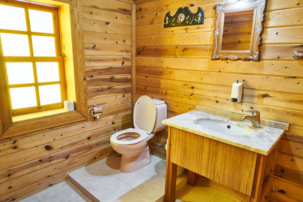 lavabo rústico com paredes em madeira com um espelho de moldura vintage e objetos decorativos em cor branca. 
