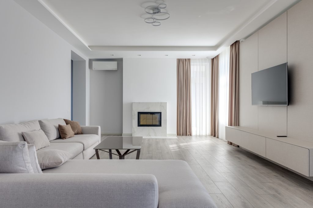 Decoração de uma sala minimalista que conta com cores pastéis na parede e também nos móveis. A imagem contém uma sala com um sofá, um rack com a TV pendurada e poucos objetos de decoração.