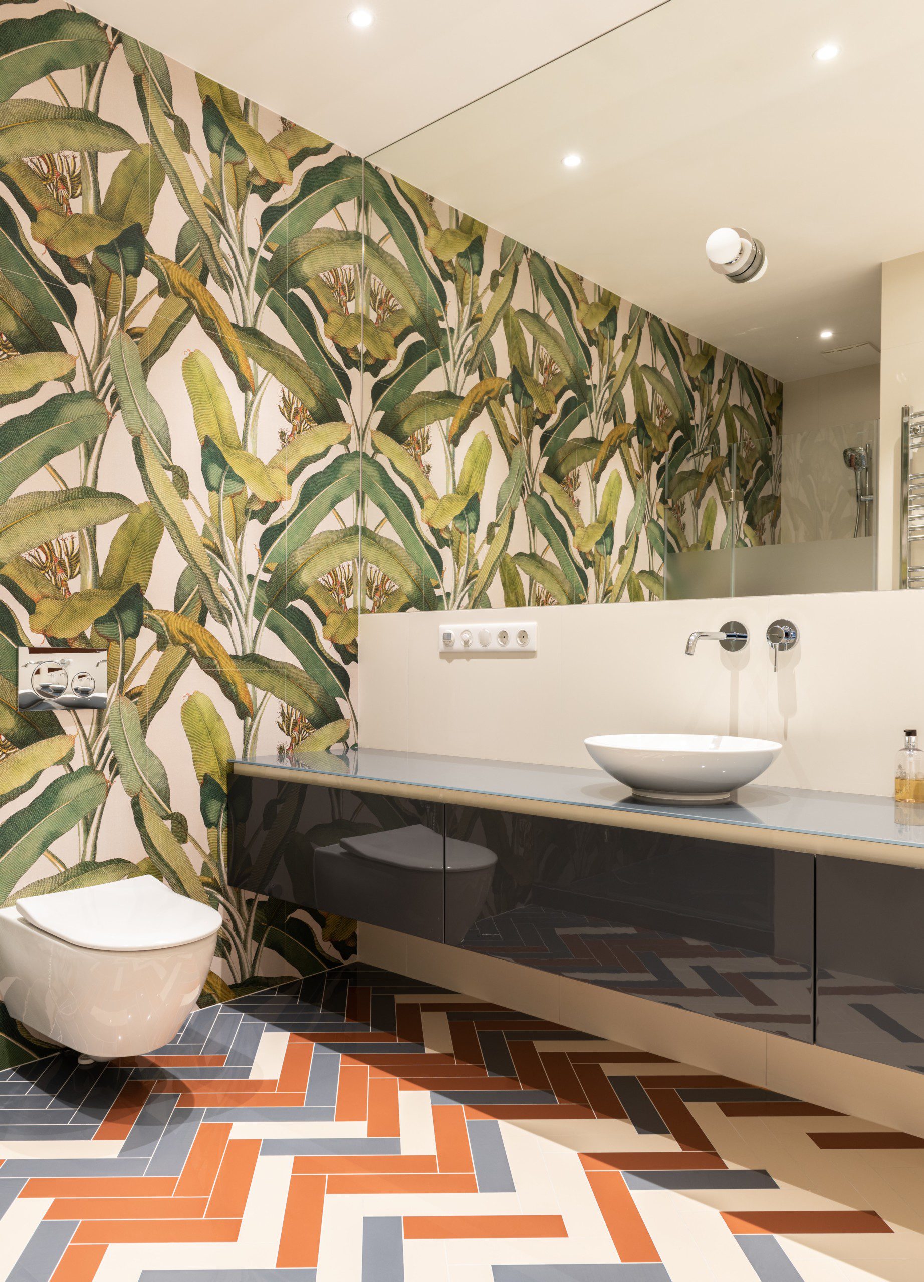 Imagem de um lavabo com uma parede toda personalizada com plantas, uma pia com gabinete preto e um vaso sanitário branco. O lavabo conta com um grande, ocupando toda a parede acima da pia.