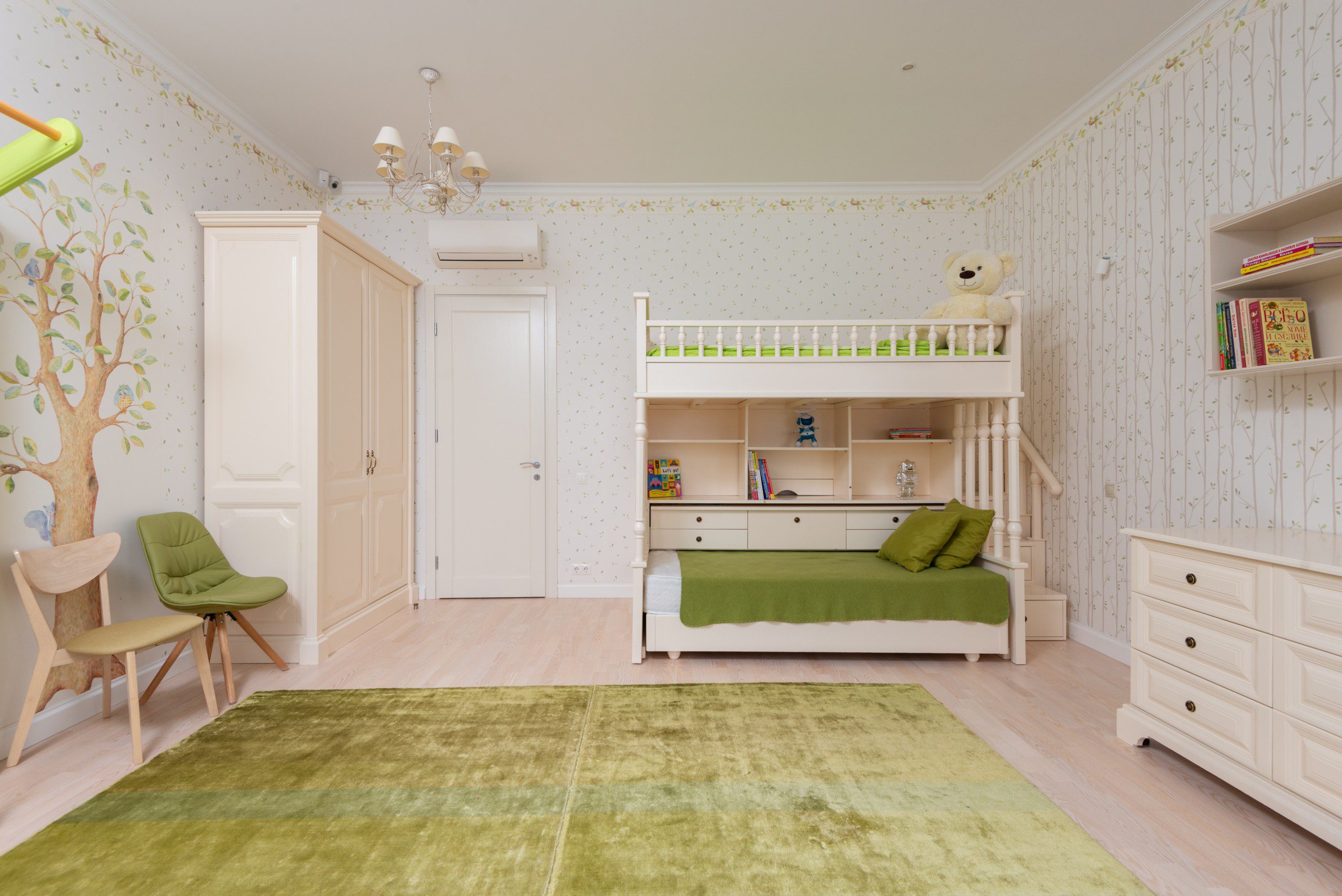 Decoração de quarto infantil em tons de bege e verde com tapete decorativo e papel de parede com árvore e folhas.
