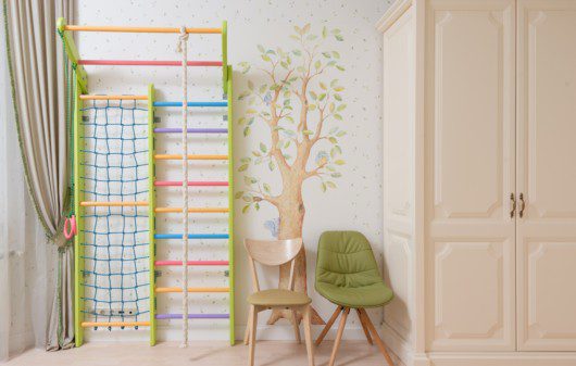 Decoração de quarto infantil em tons claros e verdes, adesivos de parede com uma árvore e folhas decorativas, além de móveis em cor bege.