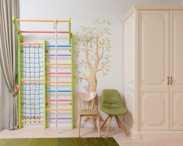 Decoração de quarto infantil em tons claros e verdes, adesivos de parede com uma árvore e folhas decorativas, além de móveis em cor bege.
