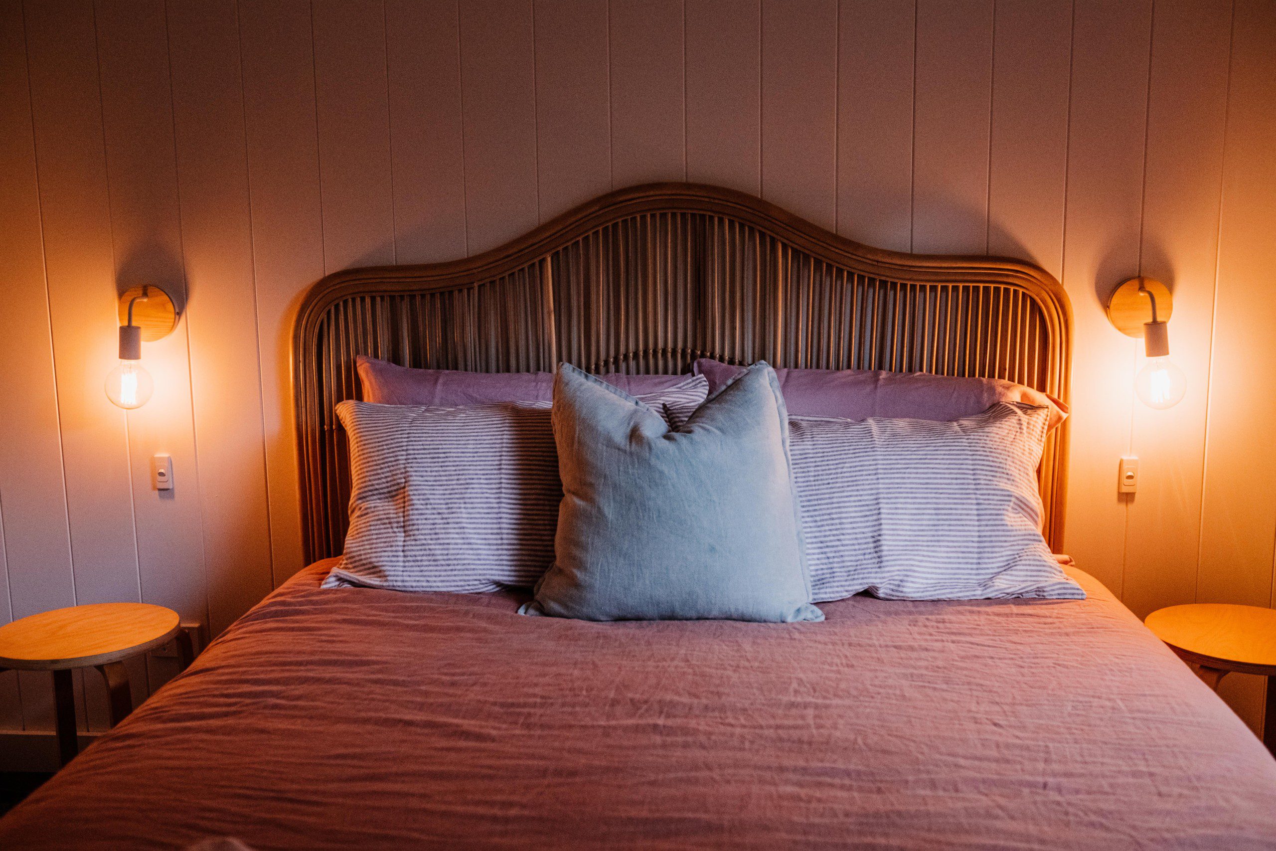Imagem da cabeceira de um quarto de casal com duas luminárias acessas penduradas na parede. 