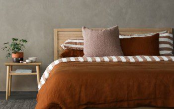 quarto simples bem decorado, com uma cama de casal com roupa de cama em tons marrons e uma mesa de cabeceira ao lado