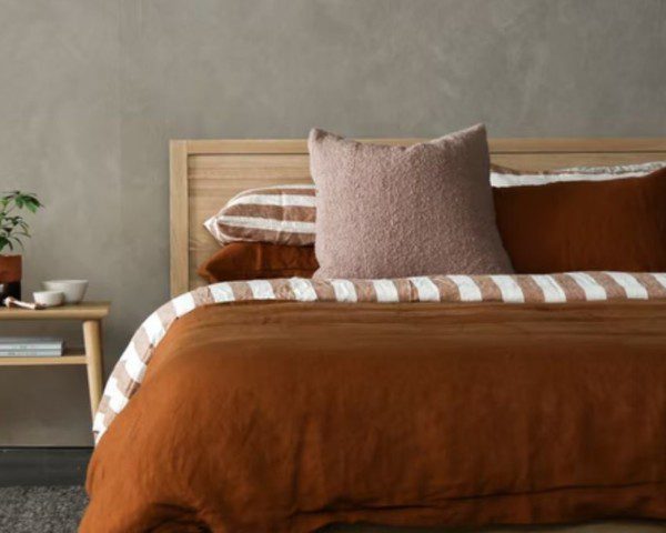 quarto simples bem decorado, com uma cama de casal com roupa de cama em tons marrons e uma mesa de cabeceira ao lado