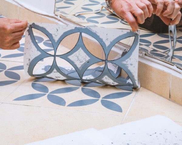 Foto que ilustra matéria sobre como fazer stencil mostra um detalhe de um molde de stencil sendo retirado de um piso após a aplicação de uma tinta azul.