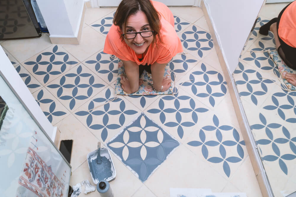 Foto que ilustra matéria sobre como fazer stencil mostra uma mulher agachada, sorrindo, após aplicar a técnica para pintar um piso.