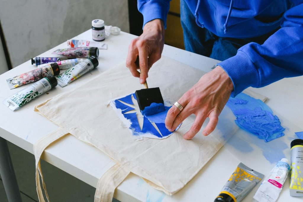 Foto que ilustra matéria sobre como fazer stencil mostra um homem pintando uma bolsa de pano com a técnica.