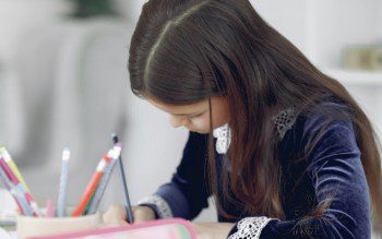 Foto que ilustra matéria sobre escolas em São Bernardo do Campo mostra uma menina sentada à mesa de uma escola enquanto escreve.