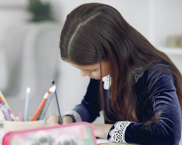 Foto que ilustra matéria sobre escolas em São Bernardo do Campo mostra uma menina sentada à mesa de uma escola enquanto escreve.