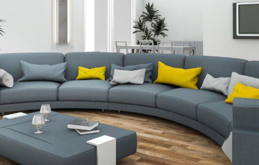 Sofá curvo cinza com almofadas brancas e amarelas e uma mesa de centro da cor do sofá