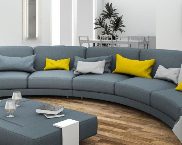 Sofá curvo cinza com almofadas brancas e amarelas e uma mesa de centro da cor do sofá