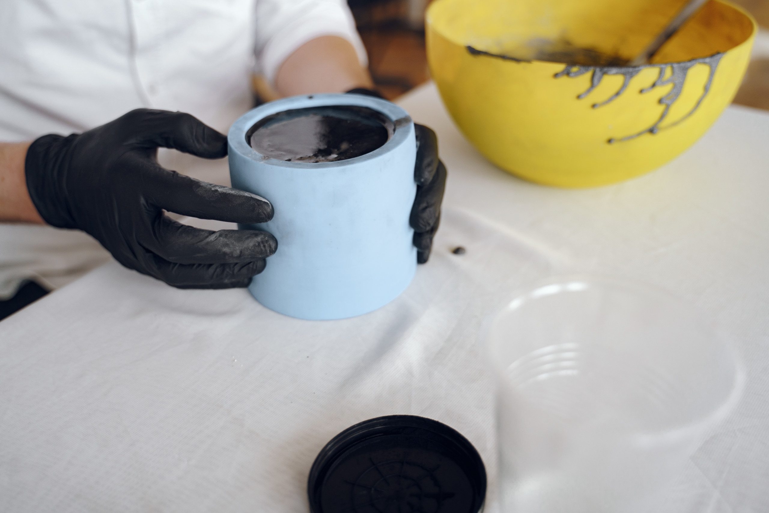 Homem de camisa branca e luvas pretas fazendo uma vaso de cimento.
