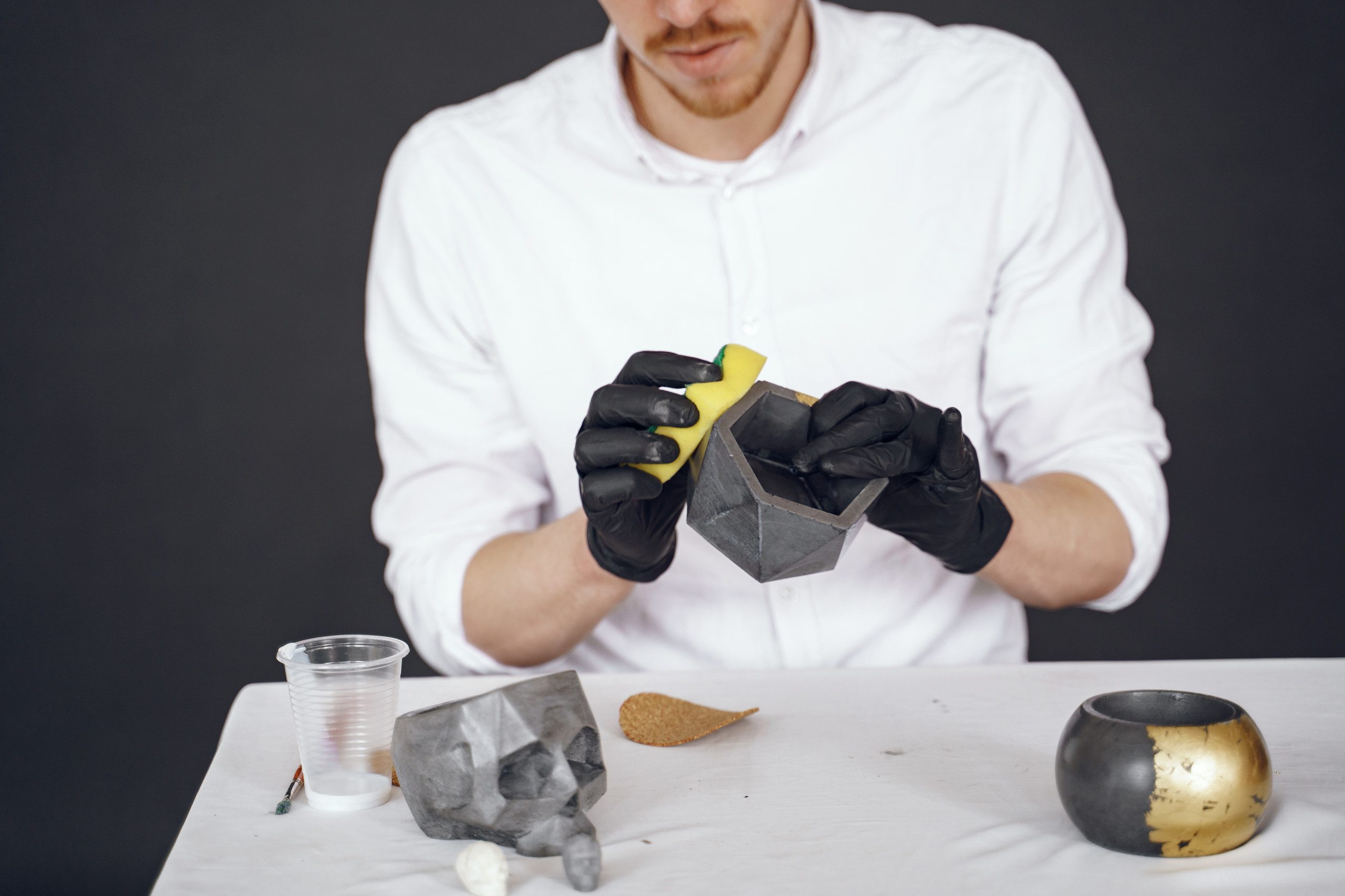 Imagem de um homem de camisa branca utilizando uma esponja para dar acabamento ao vaso de cimento. 