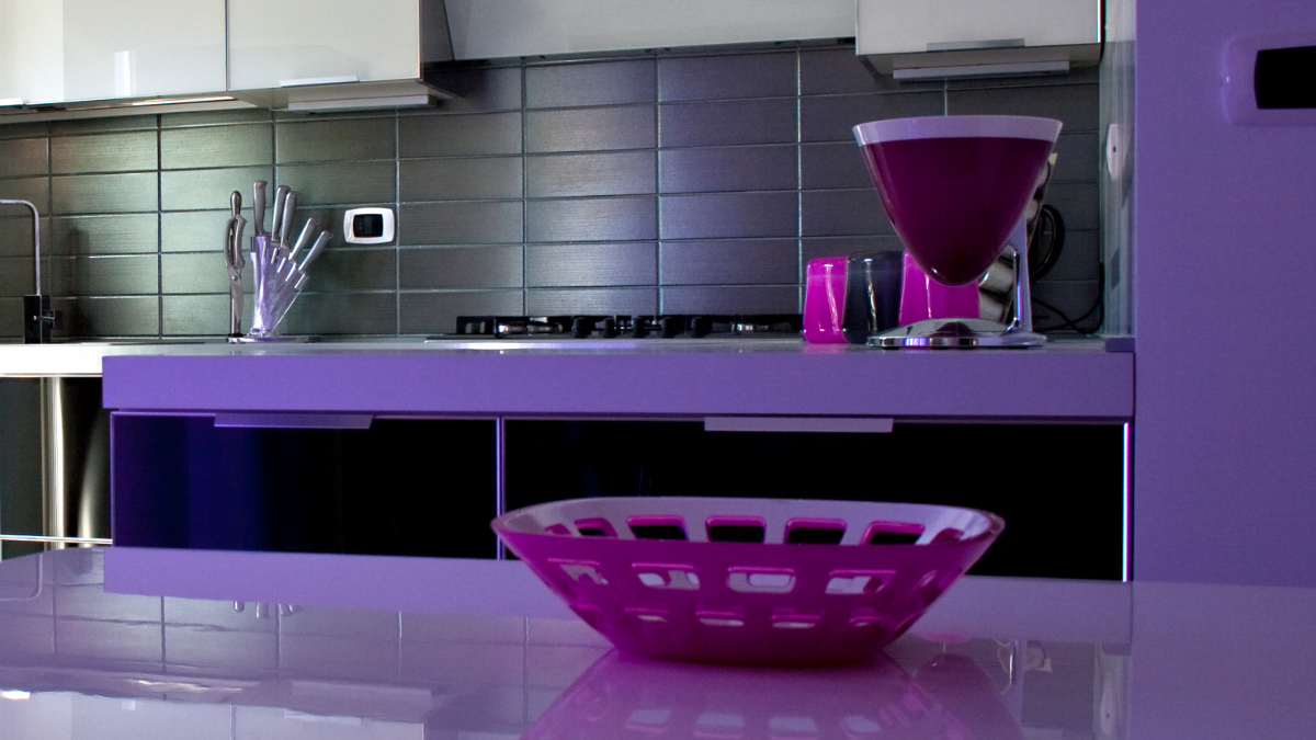 bowl de frutas em cima de uma bancada de cozinha, ao lado de uma taça. Todo o espaço é lilás