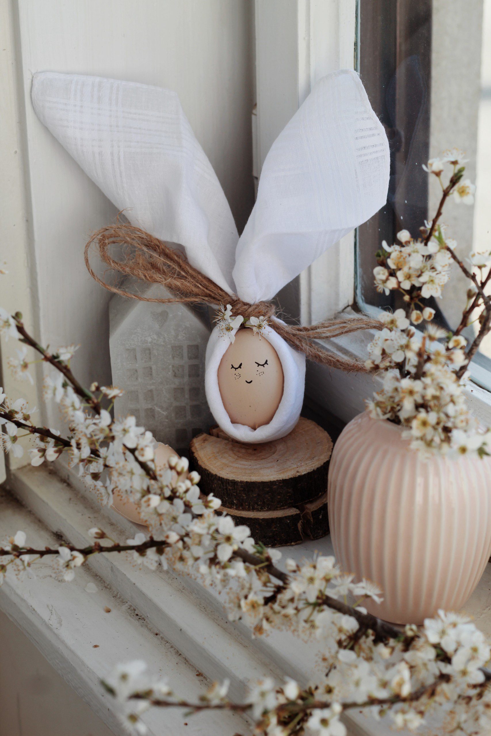 Imagem de um espaço com decoração de páscoa. É possível ver um ovo, enrolado com guardanapo de orelha de coelho