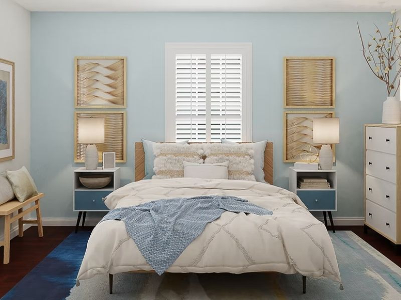 Quarto com paredes e mesa de cabeceira na cor azul, cama de casal com roupa de cama branca e duas janelas nas paredes de fundo.