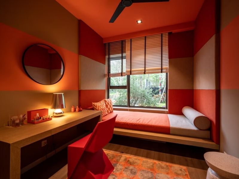 Quarto de solteiro todo vermelho, com cama encostada na parede, escrivaninha, espelho e janela ampla ao lado da cama.