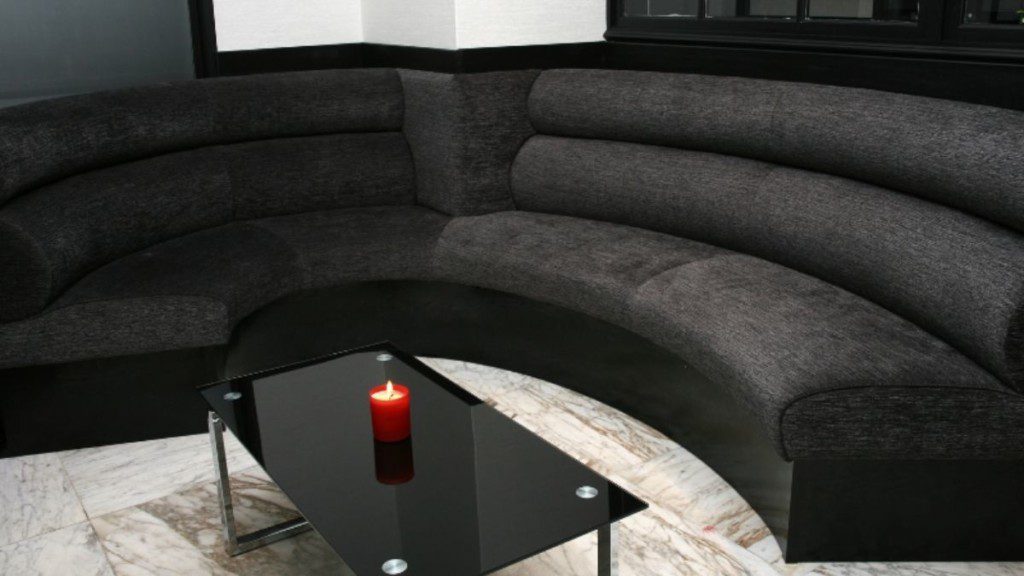 sofá curvo preto com mesa de centro também na cor preta, vela vermelha em cima e chão em tom branco acinzentado