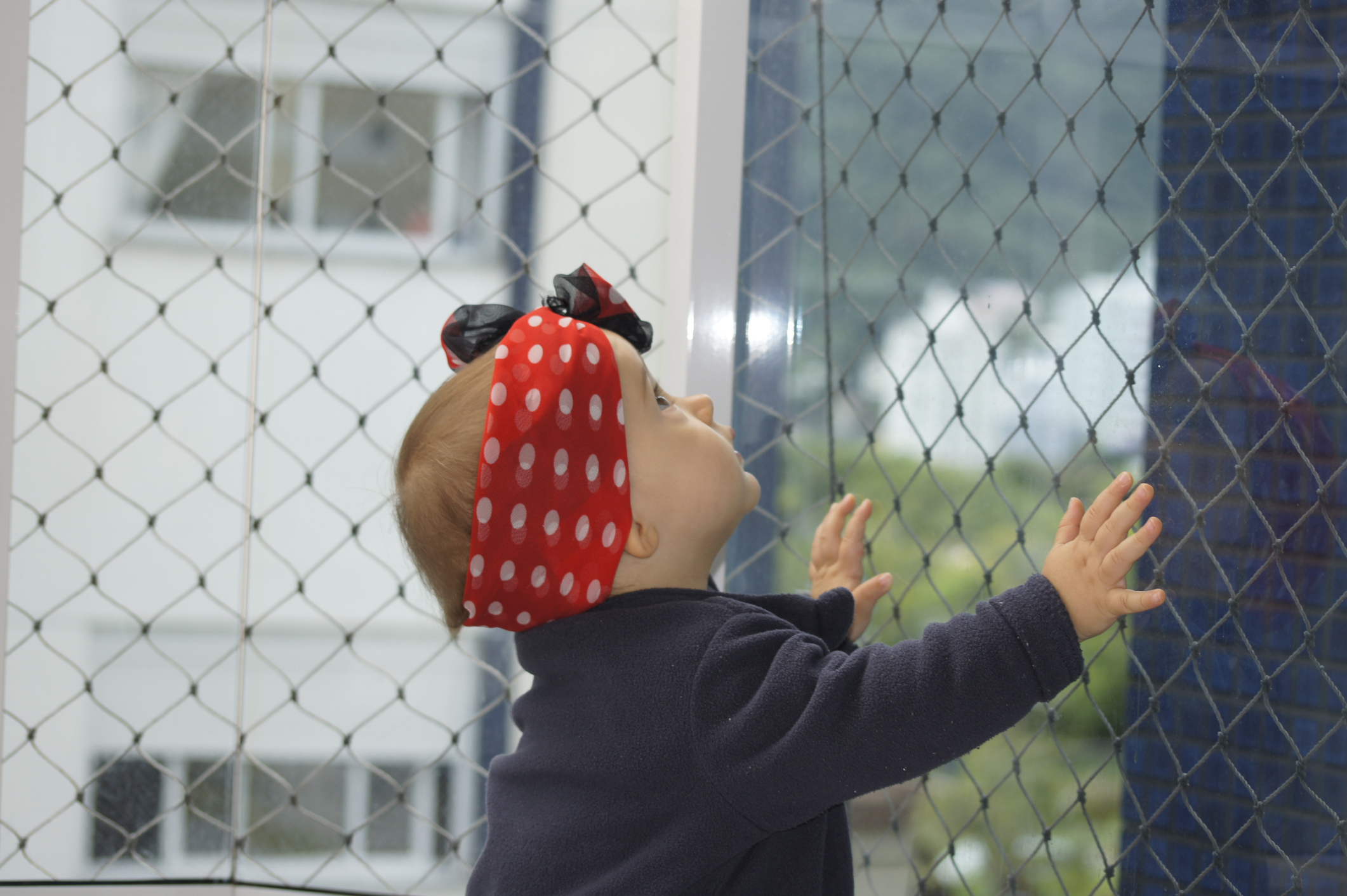 Imagem de uma criança agarrada em uma tela de proteção para varanda. 