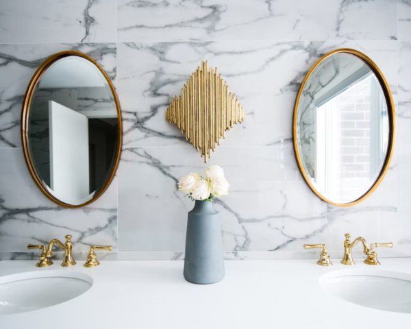 Duas pias brancas, dois espelhos redondos na parede, que é estilizada em mármore. Capa do conteúdo sobre modelos de pia para banheiro