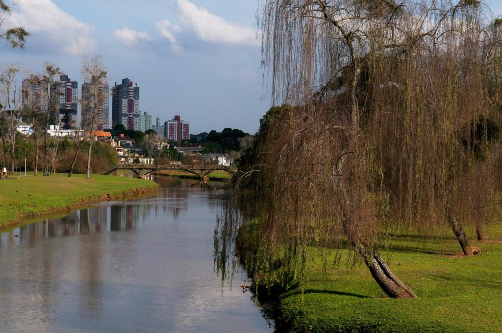 Foto que ilustra matéria sobre Parques em Curitiba mostra um riacho com uma ponte do Parque Barigui