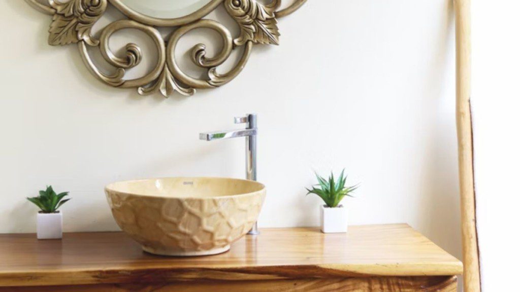 imagem de uma pia dourada esculpida para banheiro, em cima de um móvel de madeira com duas plantas suculentas pequenas, uma de cada lado
