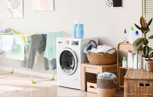 A imagem mostra uma área de serviço com máquina de lavar roupa e cestos de roupa feitos de madeira.