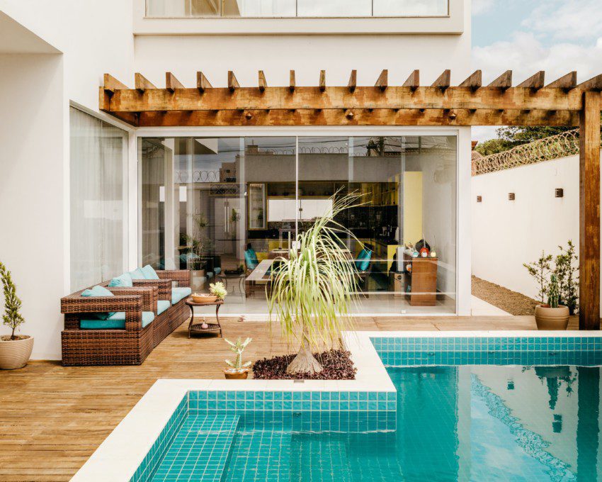 área externa de uma casa com piscina em deck de madeira, sofás e plantas em volta