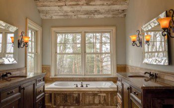 Banheiro rústico amplo com janelas largas, banheira revestida de madeira e pia de material em tom terroso