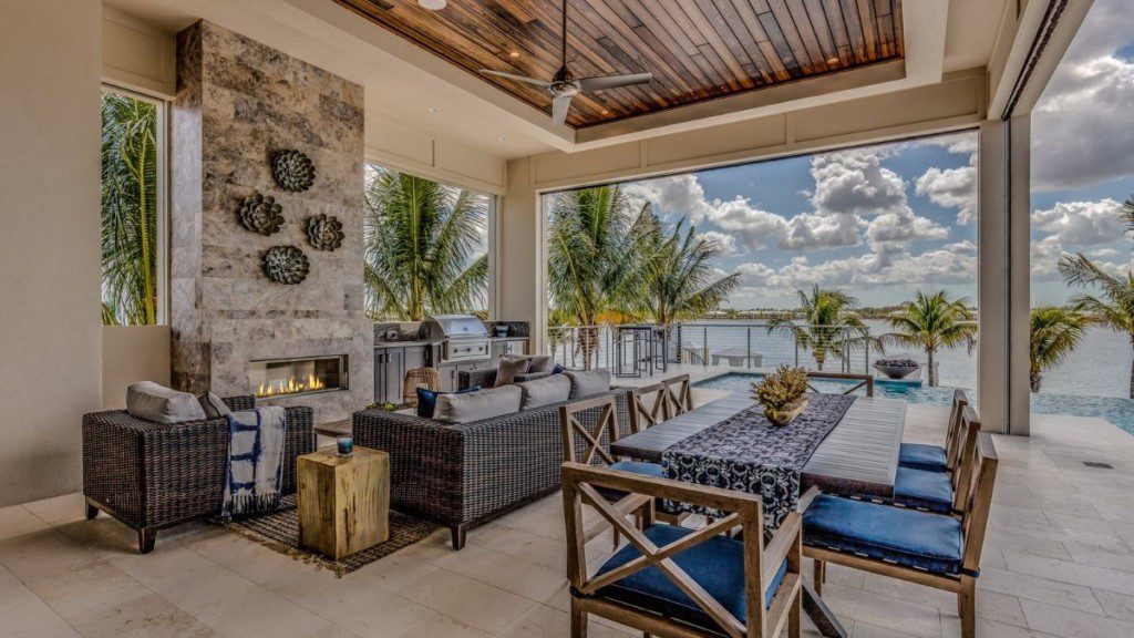 varanda de uma casa de praia, com vista para o mar no horizonte, cadeiras ao redor de uma mesa retangular, e um ambiente com lareira mais ao canto