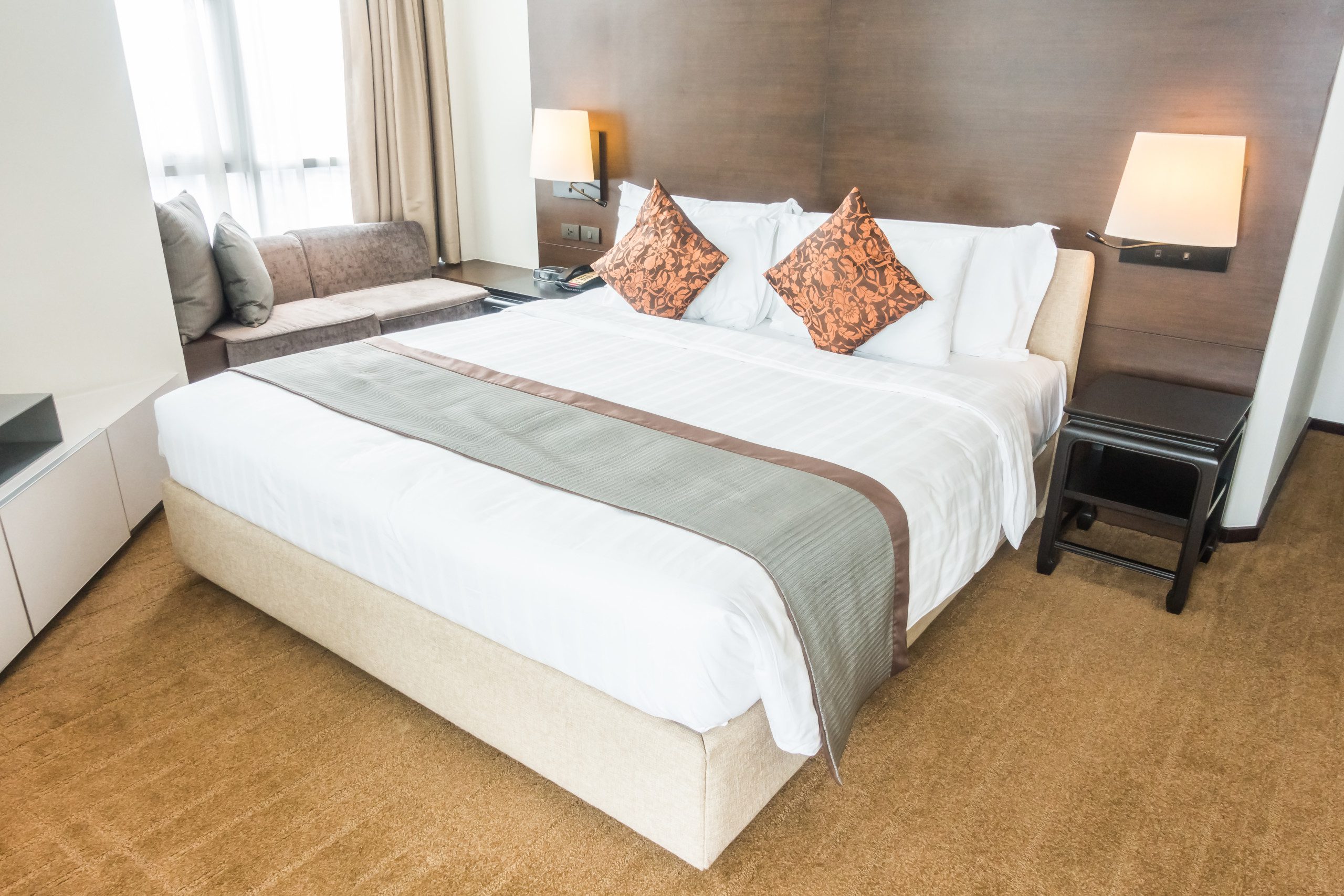 Imagem de um quarto com uma cama de casal com colcha branca e uma cabeceira estofada