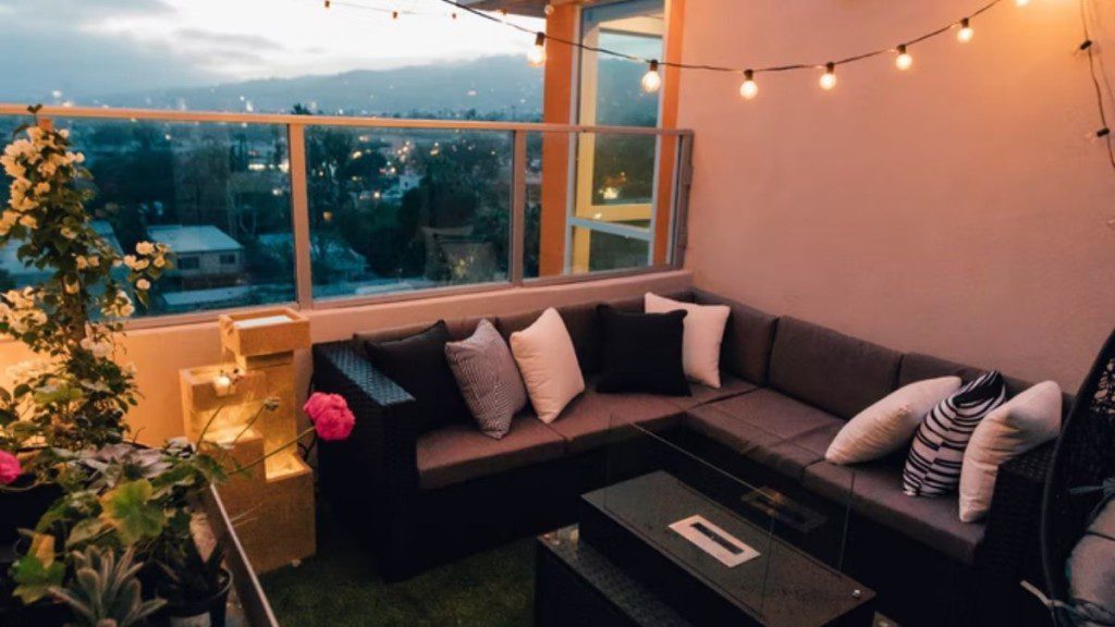 varanda com sofá de canto, plantas, luzes penduradas e almofadas