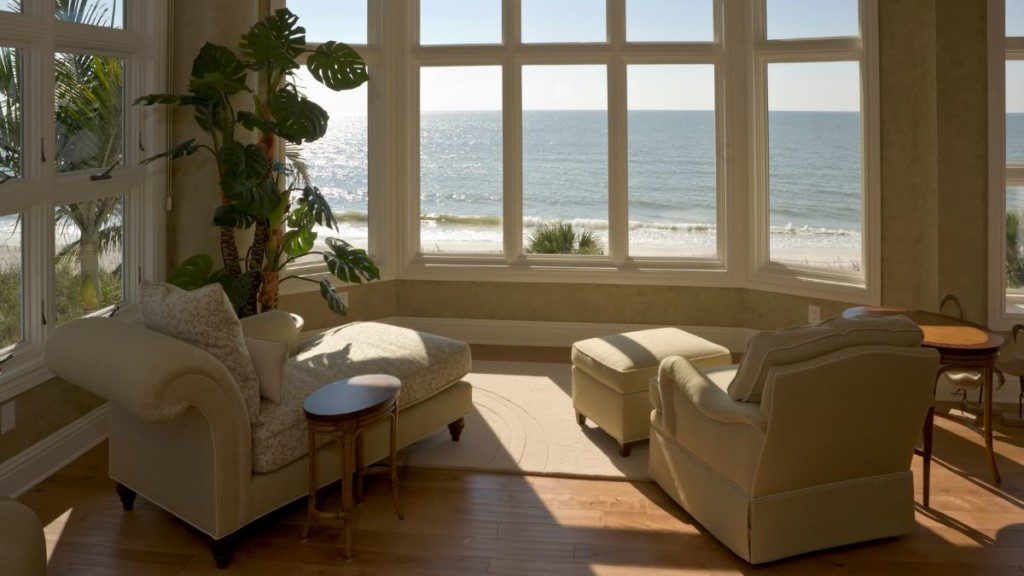 ambiente de uma casa com vista para o mar, as janelas são de vidro e há duas poltronas voltadas para o exterior