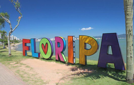 Foto que ilustra matéria sobre o que fazer em Florianópolis mostra em detalhes um letreiro com a palavra “Floripa” escrita em letras coloridas à beira de uma das praias da cidade.