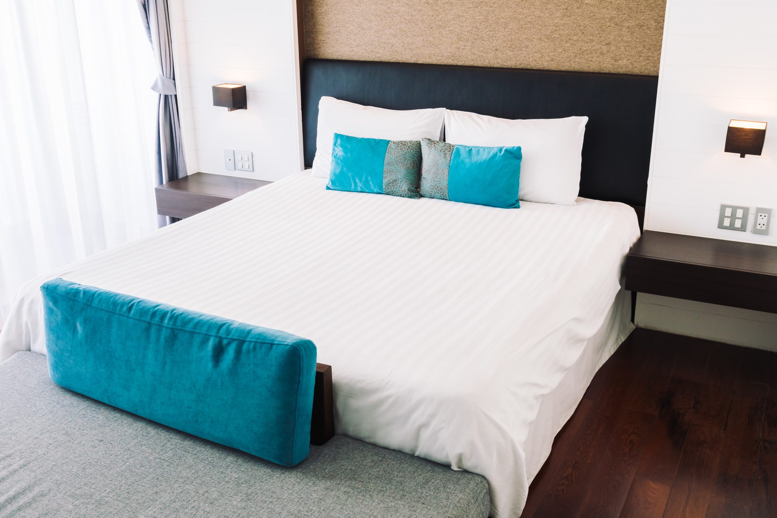 Foto de um quarto com uma cama com colcha branca e almofadas azuis e uma cabeceira preta.