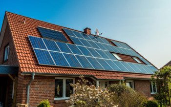 Foto que ilustra matéria sobre casas sustentáveis mostra uma casa vista de lado, com detalhe para o seu telhado quase que totalmente coberto por painéis de captação da luz solar para transformação em energia fotovoltaica.