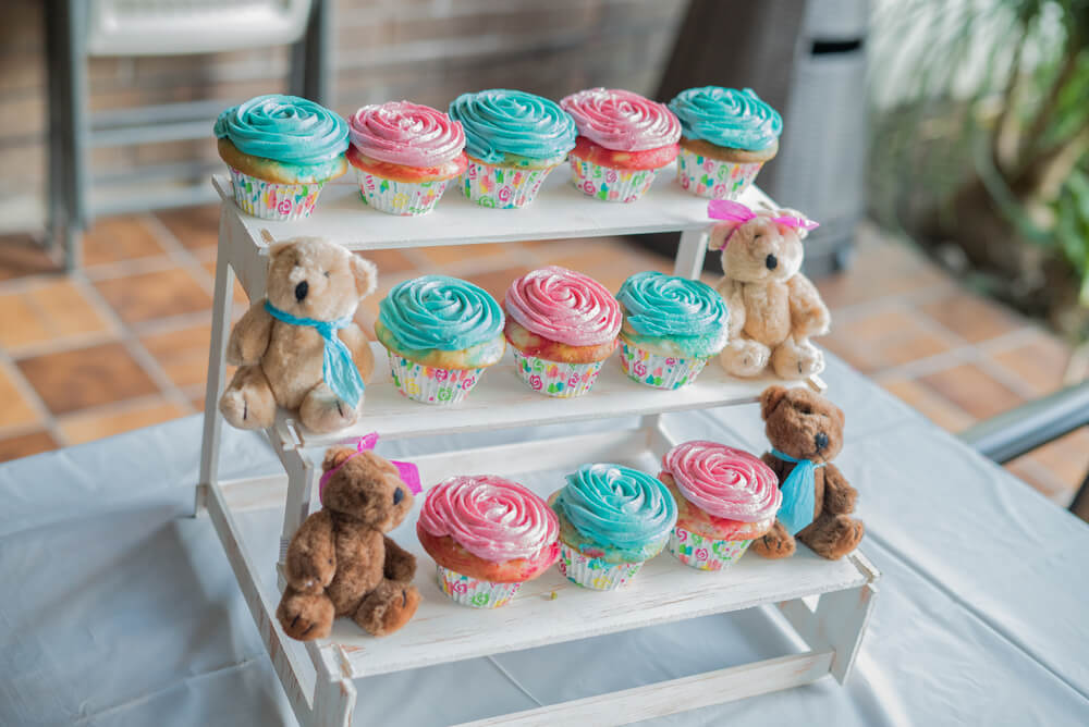 A imagem mostra uma estante com vários cupcakes e ursinhos. Os ursos são marrons e beges. Os cupcakes são rosa e azul.