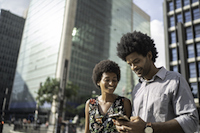 Foto que ilustra quiz de casal para o Dia dos Namorados mostra um casal andando pela cidade e olhando o celular, representando um casal que gosta de uma vida cultural intensa