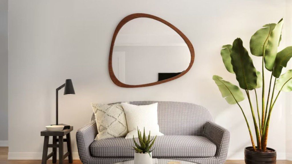 sala minimalista com sofá pequeno, espelho em formato diferente, planta e luminária