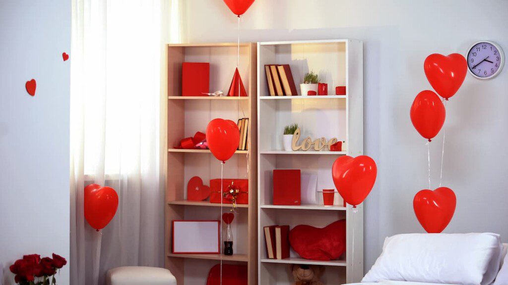 Ambiente decorado para o dia dos namorados. É possível ver uma estante branca decorada com balões em formato de coração.