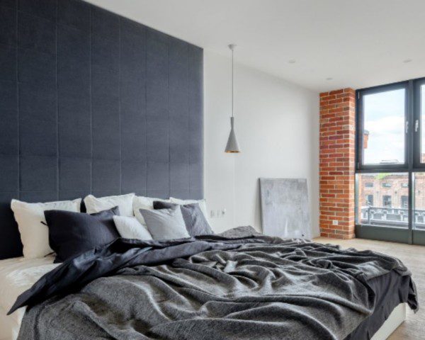 cama king size em quarto amplo em decoração industrial, com lâmpadas dos dois lados e janelas abertas de vidro