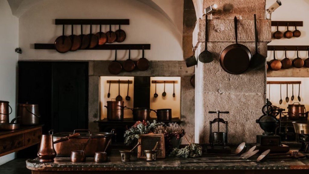 A imagem mostra uma cozinha com decoração industrial. Nela há artefatos nas paredes, móveis de madeira e antigos e iluminação ambientada.