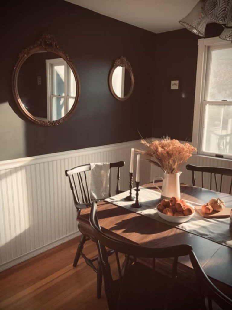 sala de jantar com mesa de madeira, cadeiras de madeira, arranjo de flores no centro da mesa e espelhos redondos na parede