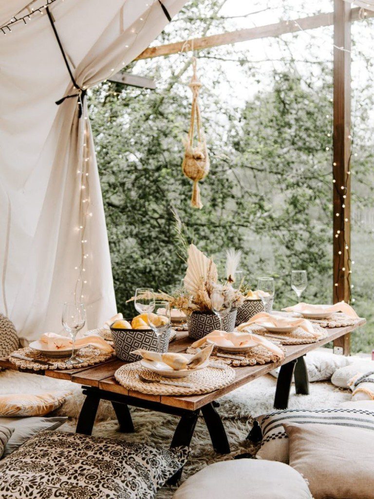 ambiente decorado com pufes, mesa de centro com pratos e jogo americano e a cortina mostrando o lado de fora todo arborizado