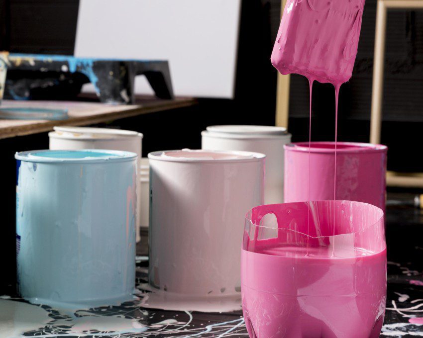 Imagem de um pincel escorrendo tinta rosa e diversos potes com tintas coloridas.