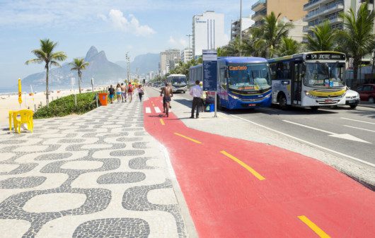 Foto que ilustra matéria sobre o custo de vida no Rio de Janeiro mostra um pedaço do calçadão da Avenida Vieira Souto, em Ipanema à esquerda, com uma pista de ciclovia ao centro e a faixa de tráfego à direita, onde aparecem dois ônibus.