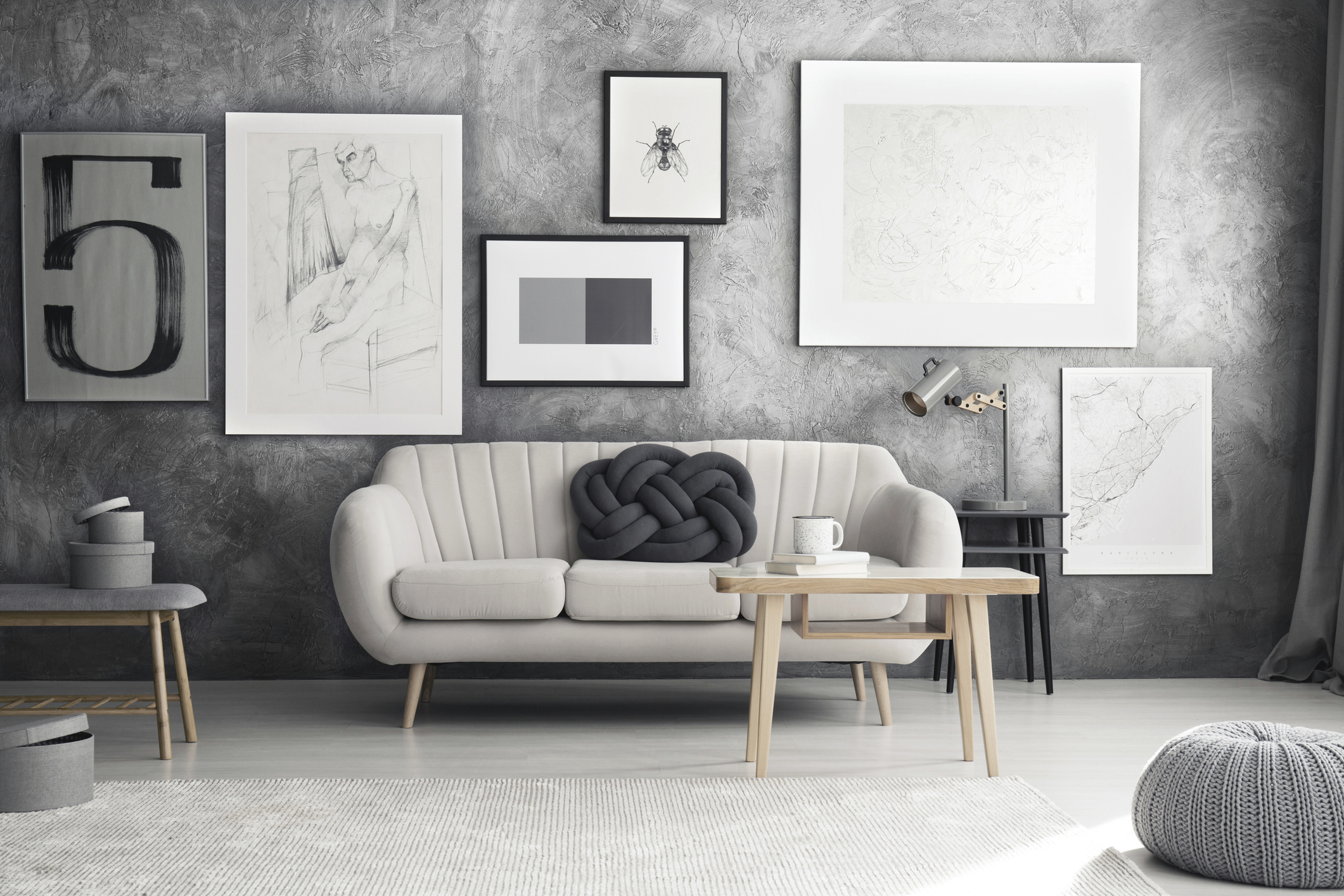 Imagem de uma sala de estar com sofá bege e uma almofada de nó cinza decorando o sofá.