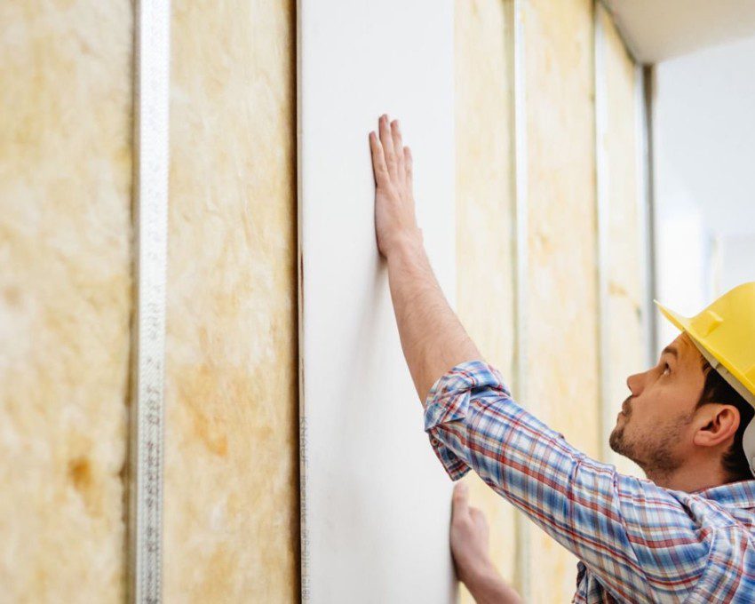 Imagem de um homem fazendo a instalação de uma parede de gesso.