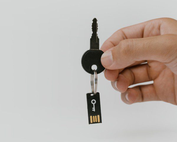 Foto de uma mão segurando uma chave de um imóvel. O chaveiro é um pendrive sinalizando segurança.